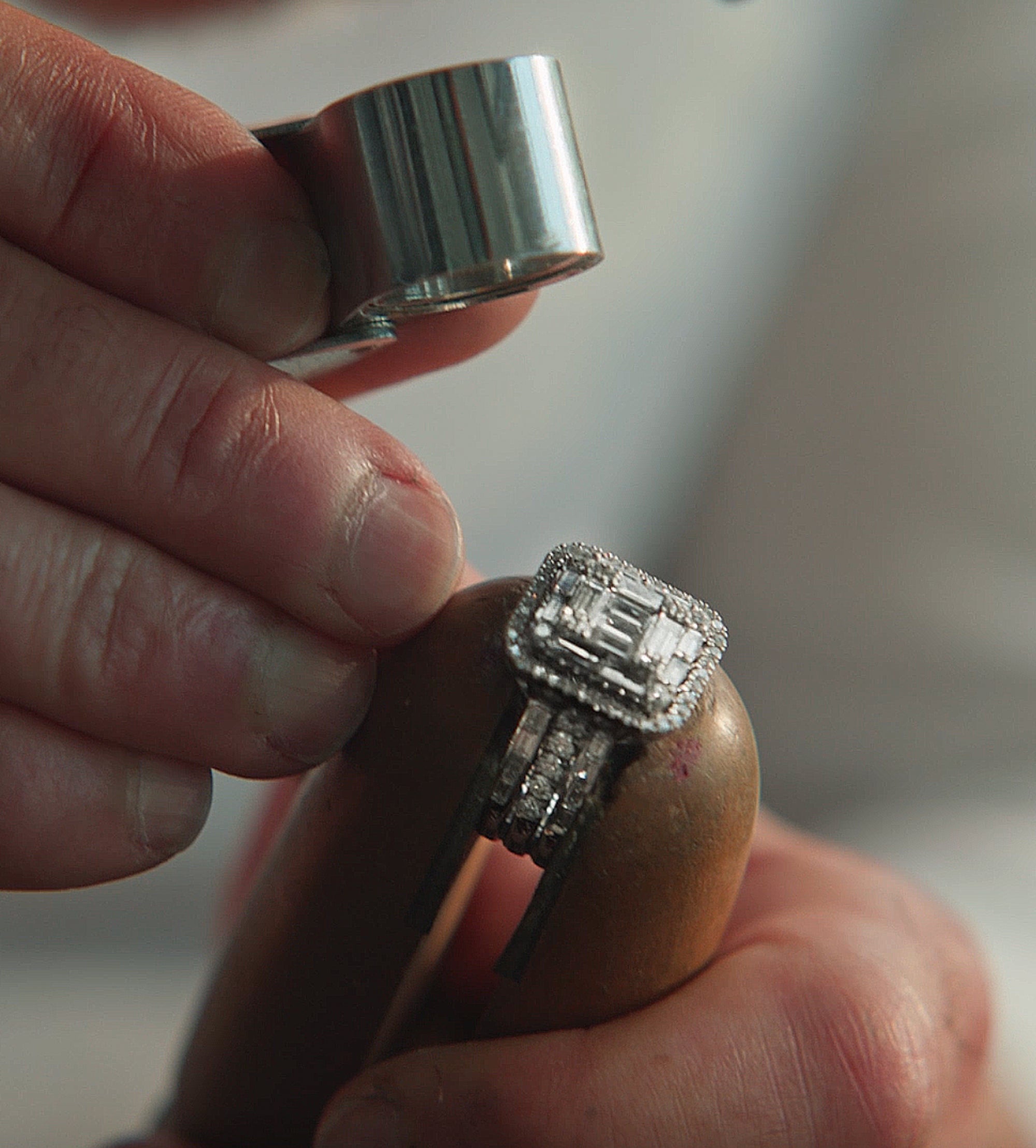 A person examines a diamond ring with a jewelers loupe, holding the ring in a wooden clamp, focusing on its intricate design and sparkling stones.