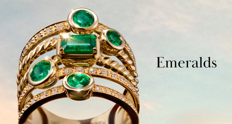 A gold ring featuring multiple sparkling green emeralds and small diamonds, with the word “Emeralds” written beside it against a soft sky background.
