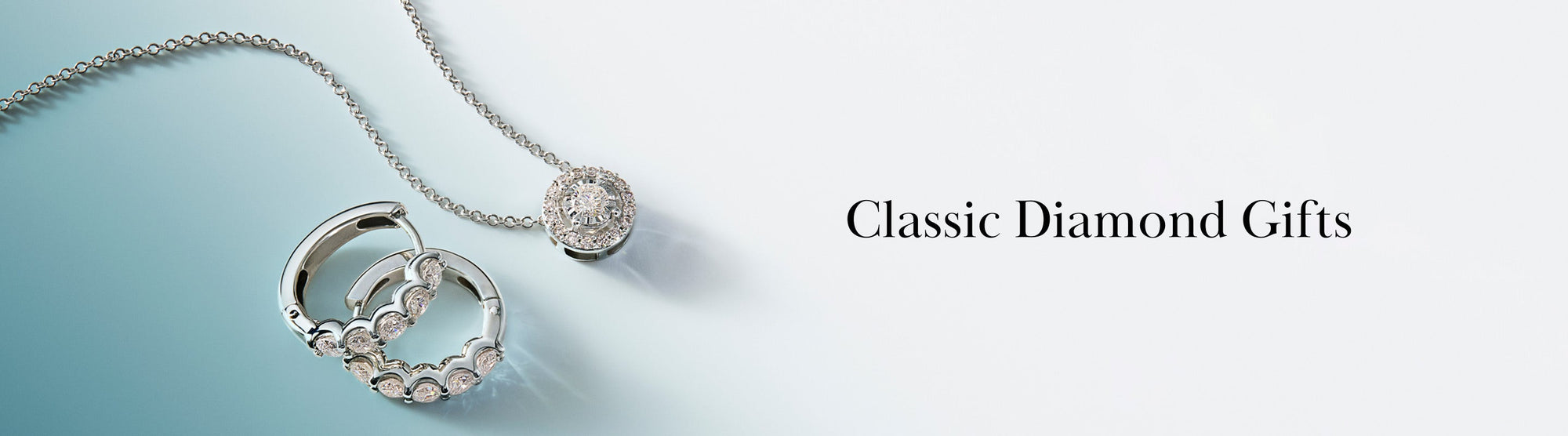 A silver necklace with a round diamond pendant and silver hoop earrings with diamond accents, displayed on a light blue and white background next to the text Classic Diamond Gifts.
