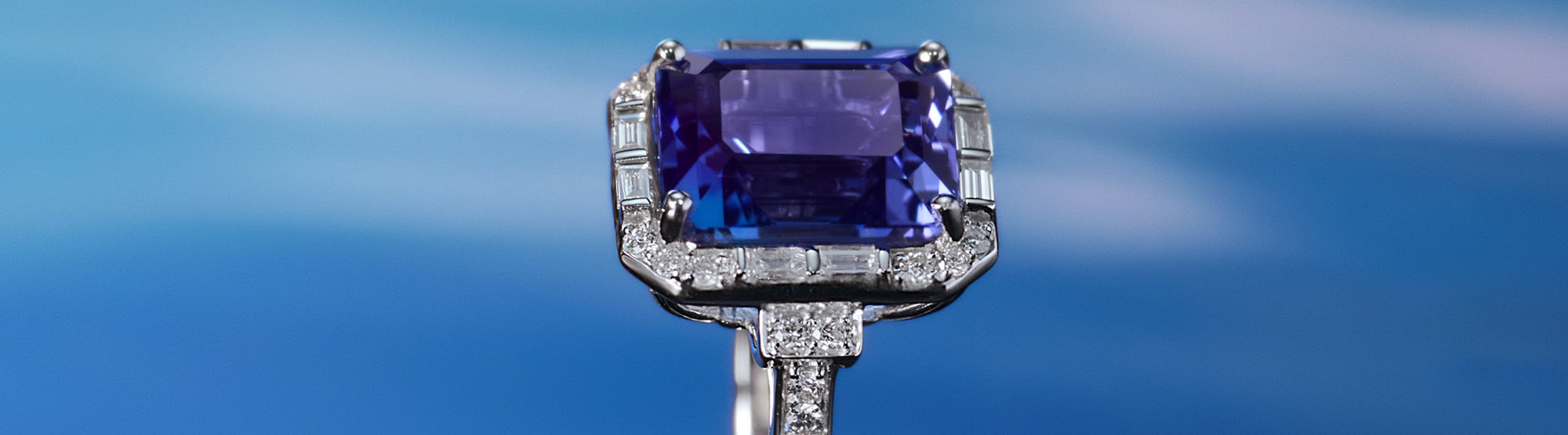 A tanzanite necklace and ring with double halos of diamonds are displayed on a satin surface beside a box, with the word Tanzanite written on the right.