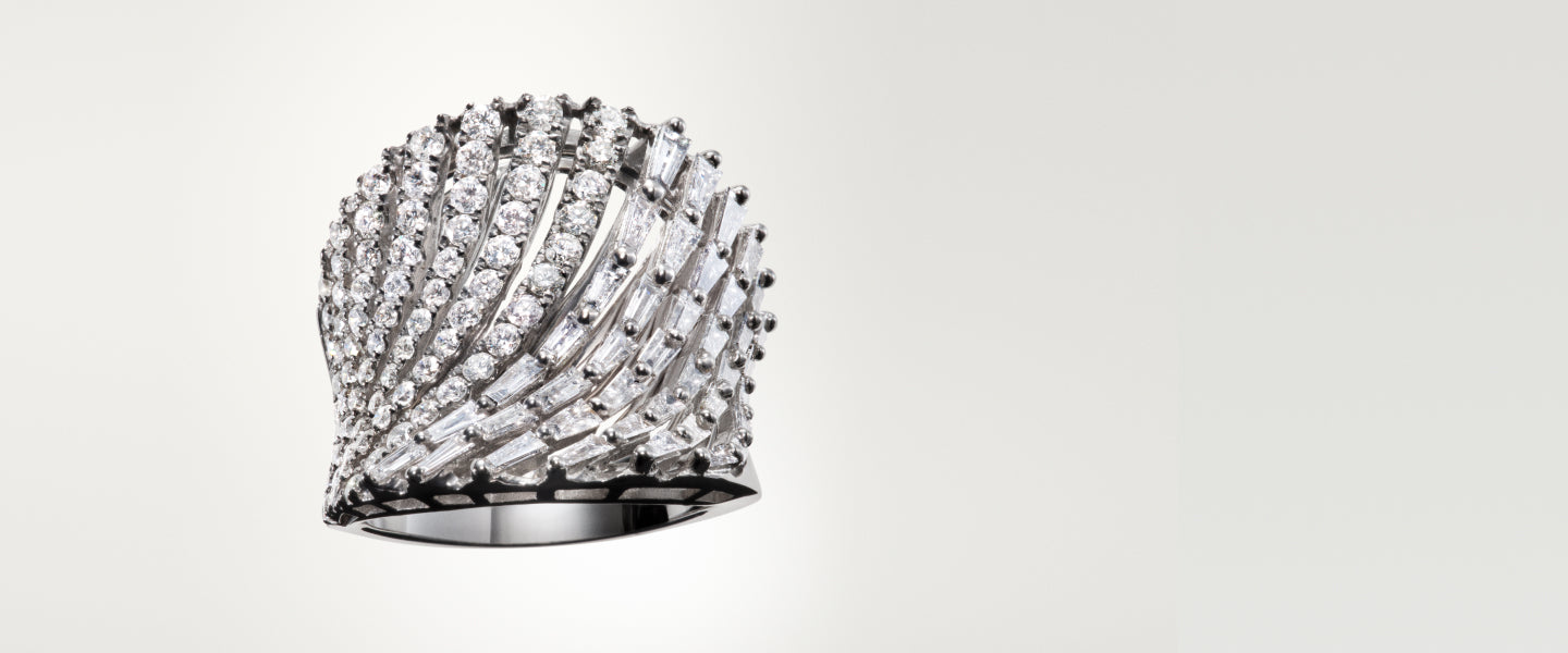 A silver ring featuring multiple rows of sparkling round and baguette-cut diamonds, elegantly arranged in a fan-like, sculptural design against a plain, light background.
