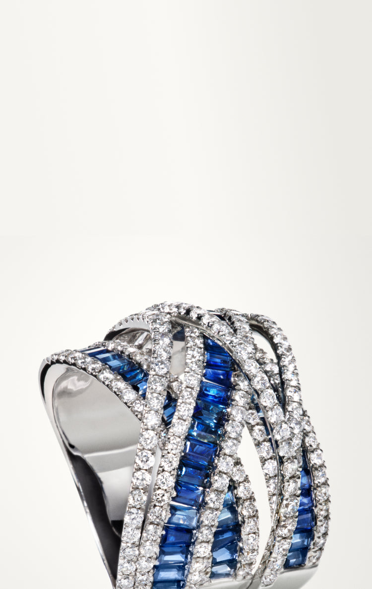 A silver ring with intertwining bands, adorned with rows of small white diamonds and rectangular blue gemstones, set against a plain white background.