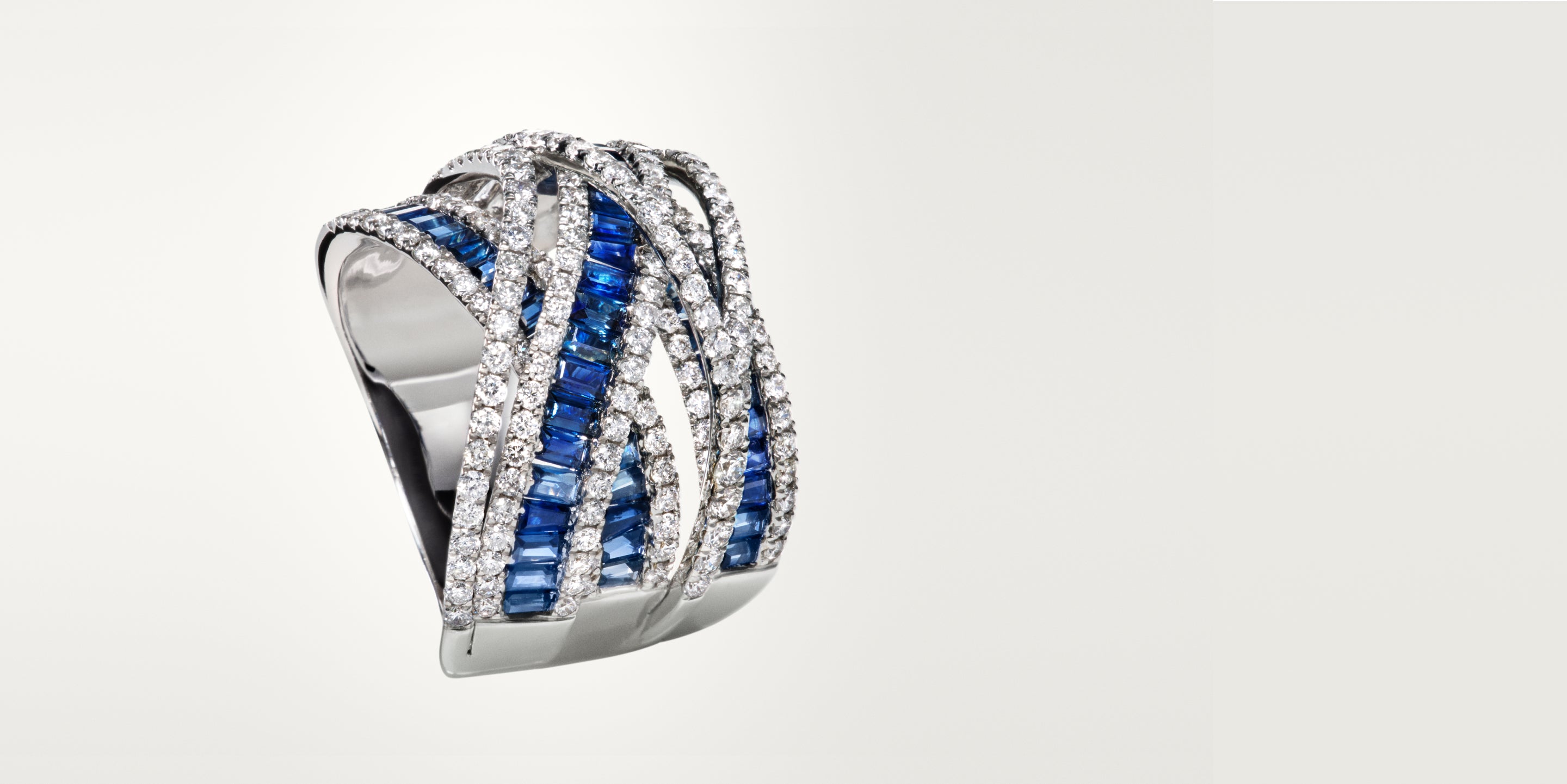 A silver ring featuring multiple intertwined bands, set with rows of blue rectangular gemstones and sparkling white diamonds, displayed against a plain white background.