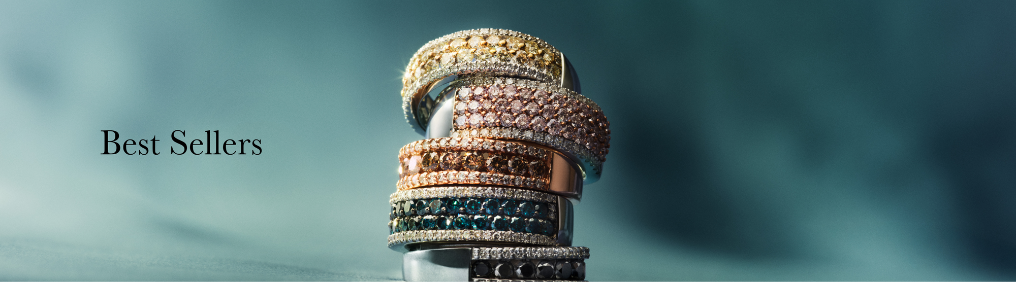 A stack of sparkling gemstone and diamond rings in gold, rose gold, and silver finishes on a blue background, with the text Best Sellers on the left.