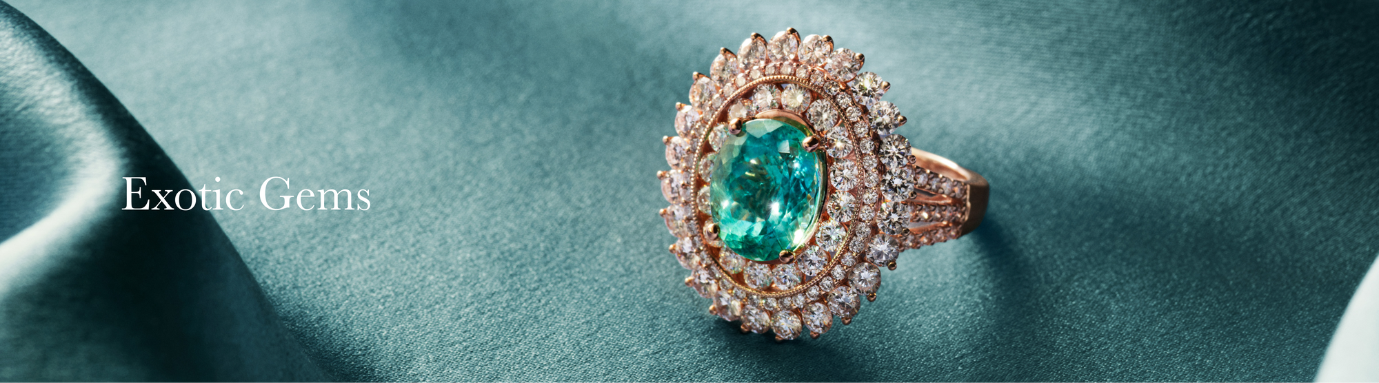 A gold ring with a large green gemstone surrounded by diamonds rests on a silky teal fabric. The text Exotic Gems appears on the left side.