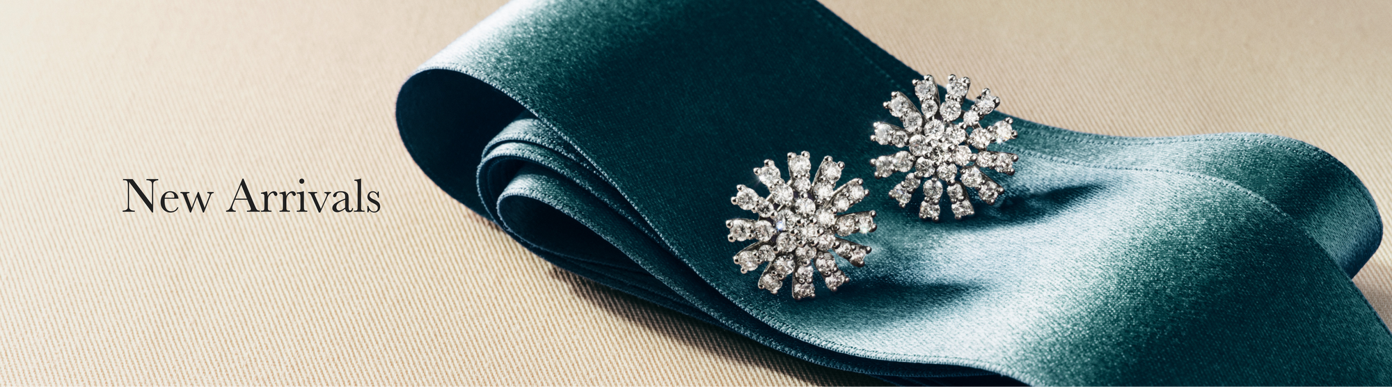 A person wearing gold rings and a bracelet touches their foot, with the words New Arrivals displayed on the left against a dark fabric background.