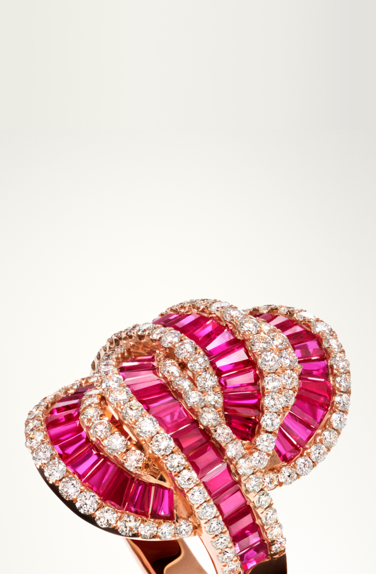 A luxurious ring featuring intertwined loops of pink gemstones and rows of sparkling white diamonds set in rose gold, displayed on a light background.